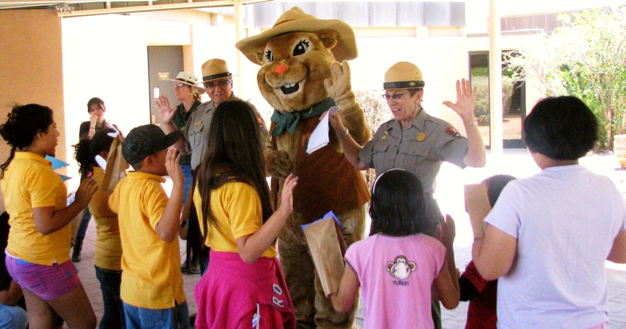 a group of children with hand raised in front of park rangers and ground squirrel mascot
